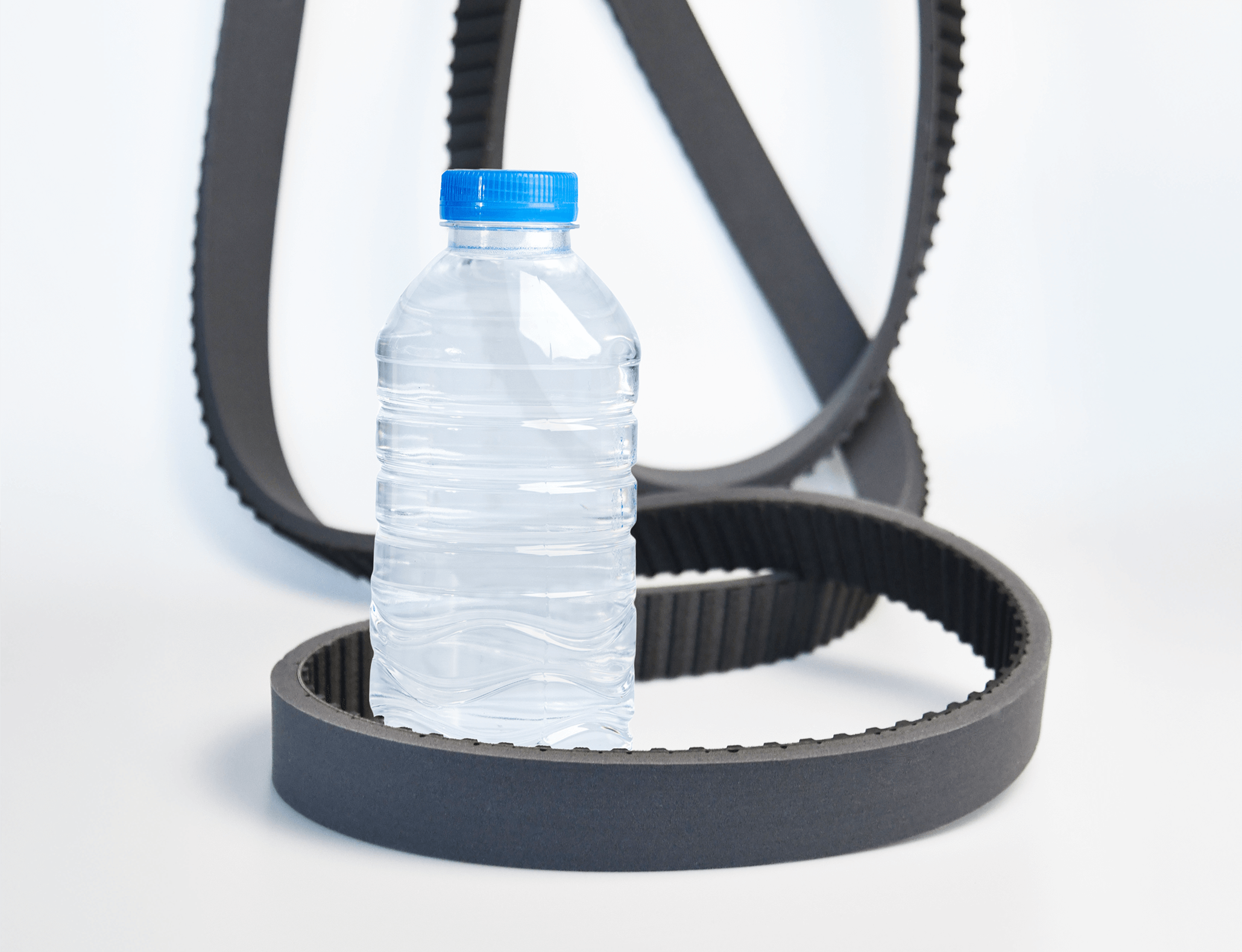 Bottle unscramblers: Belts lying on white floor around plastic bottle